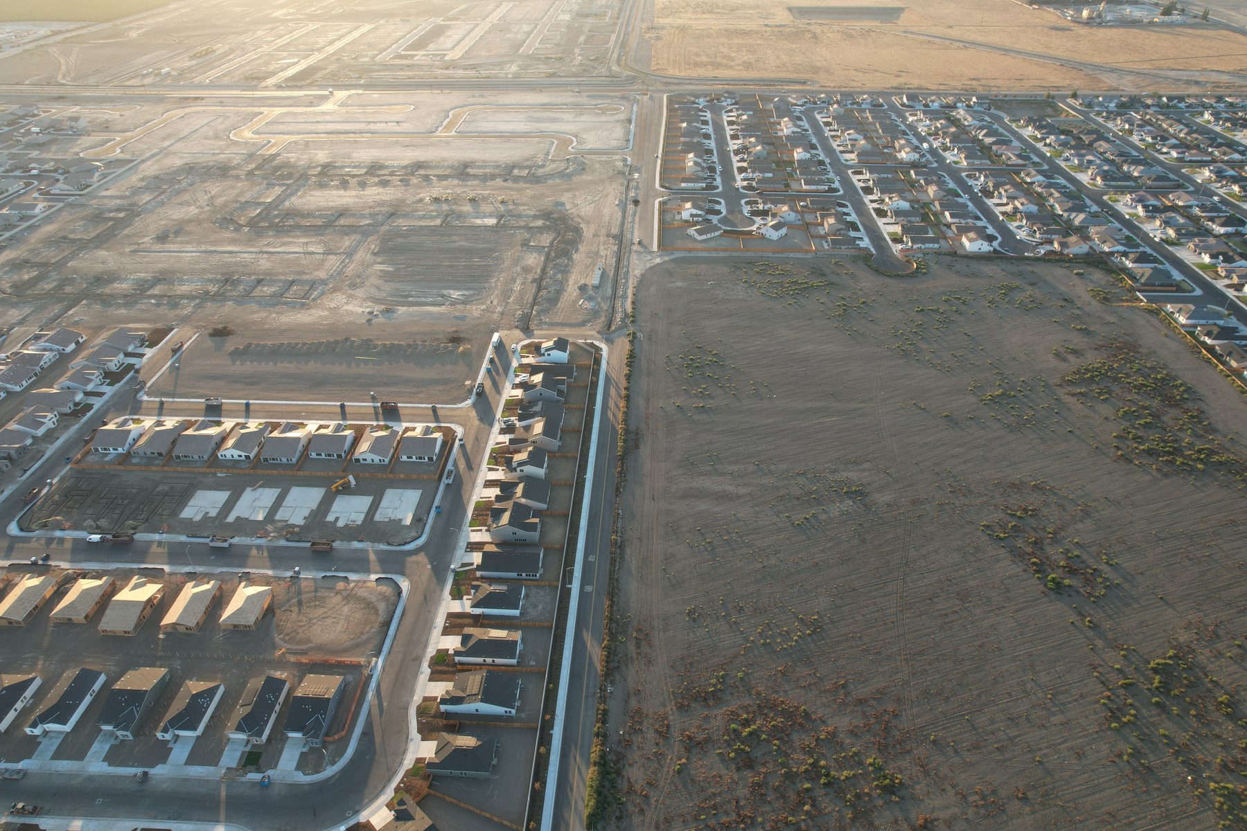 Aerial view showing raw land, graded pads, framed houses, and finished homes in one frame